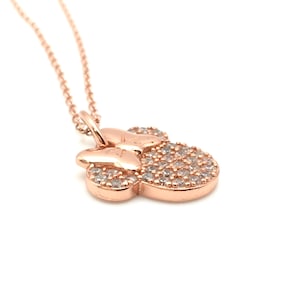 May include: A rose gold-toned necklace featuring a pendant shaped like a stylized mouse head with a bow. The pendant is encrusted with numerous small, clear, sparkling stones that cover the surface of the head and the bow, attached to a delicate chain.