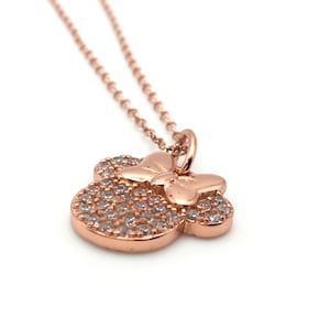 May include: A rose gold-toned necklace featuring a pendant shaped like a mouse head silhouette with a bow. The pendant is encrusted with numerous small, clear, sparkling stones across the surface of the head and includes a delicate chain.