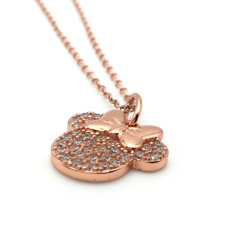 May include: A rose gold-toned necklace featuring a pendant shaped like a mouse head silhouette with a bow. The pendant is encrusted with numerous small, clear, sparkling stones across the surface of the head and includes a delicate chain.