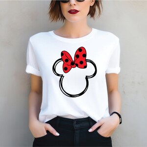 a woman wearing a white shirt with a red minnie mouse head on it
