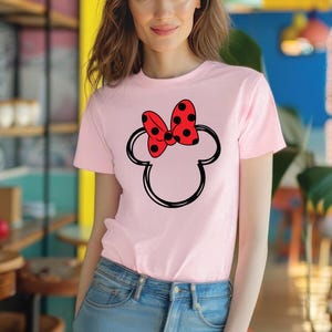 a woman wearing a pink shirt with a red minnie mouse head on it