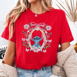 a woman wearing a red t - shirt with a picture of stitched stitching