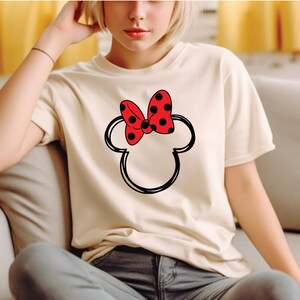 a woman sitting on a couch wearing a minnie mouse t - shirt