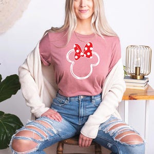 a woman sitting on a chair wearing a minnie mouse shirt