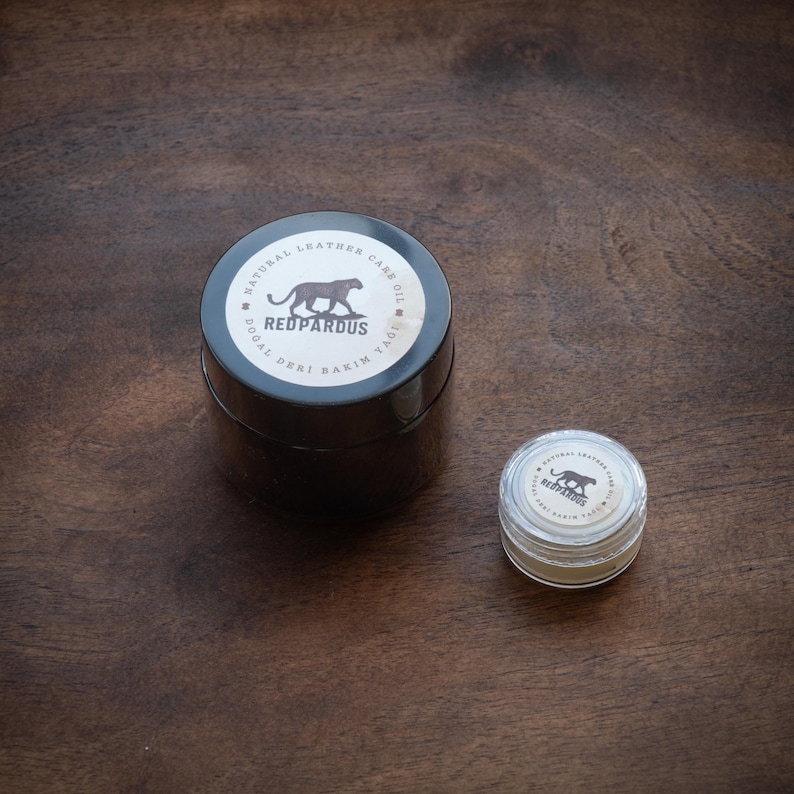 May include: Two containers of natural leather care oil. The larger container is black with a silver label that reads "Natural Leather Care Oil" and "Redpardus" with a cheetah silhouette. The smaller container is clear with a silver label that reads "Redpardus" with a cheetah silhouette.