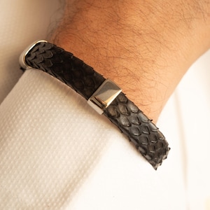 Può includere: Un braccialetto in pelle nera con una chiusura in argento. Il braccialetto è in pelle di serpente.