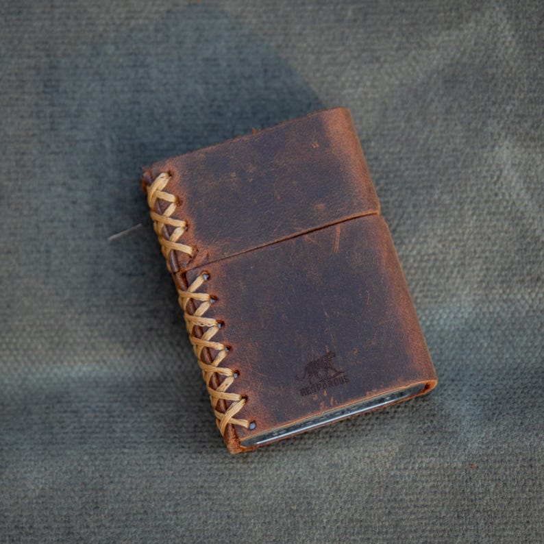 May include: A brown leather lighter case with a tan leather braided trim. The case has a logo of a stylized panther with the text "BEAST MAKERS" underneath.