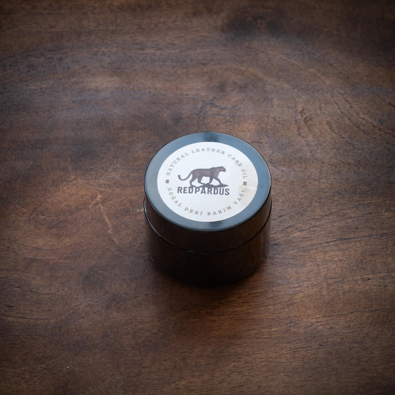 May include: A black jar with a white label that says "Natural Leather Care Oil" and "Redpardus" with a black panther illustration. The label also says "Dogal Deri Bakim Yagi" in Turkish.