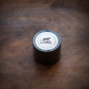 May include: A black jar with a white label that says "Natural Leather Care Oil" and "Redpardus" with a black panther illustration. The label also says "Dogal Deri Bakim Yagi" in Turkish.