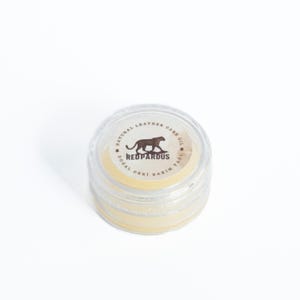 May include: A small clear jar with a yellow lid containing a natural leather care oil. The label on the jar reads "Natural Leather Care Oil, Redpardus, Dogal Deri Bakim Yagi".