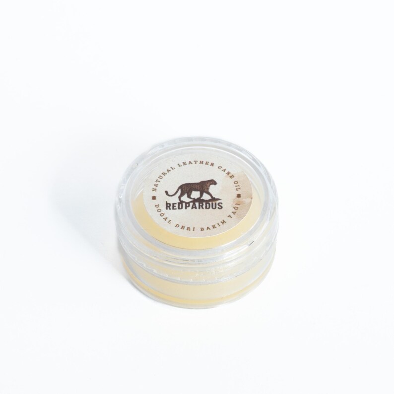 May include: A small clear jar with a yellow lid containing a natural leather care oil. The label on the jar reads "Natural Leather Care Oil, Redpardus, Dogal Deri Bakim Yagi".