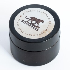 May include: A small black jar with a white label that says "Natural Leather Care Oil" and "Redpardus" with a leopard illustration. The label also says "Dogal Deri Bakim Yagi" in Turkish.