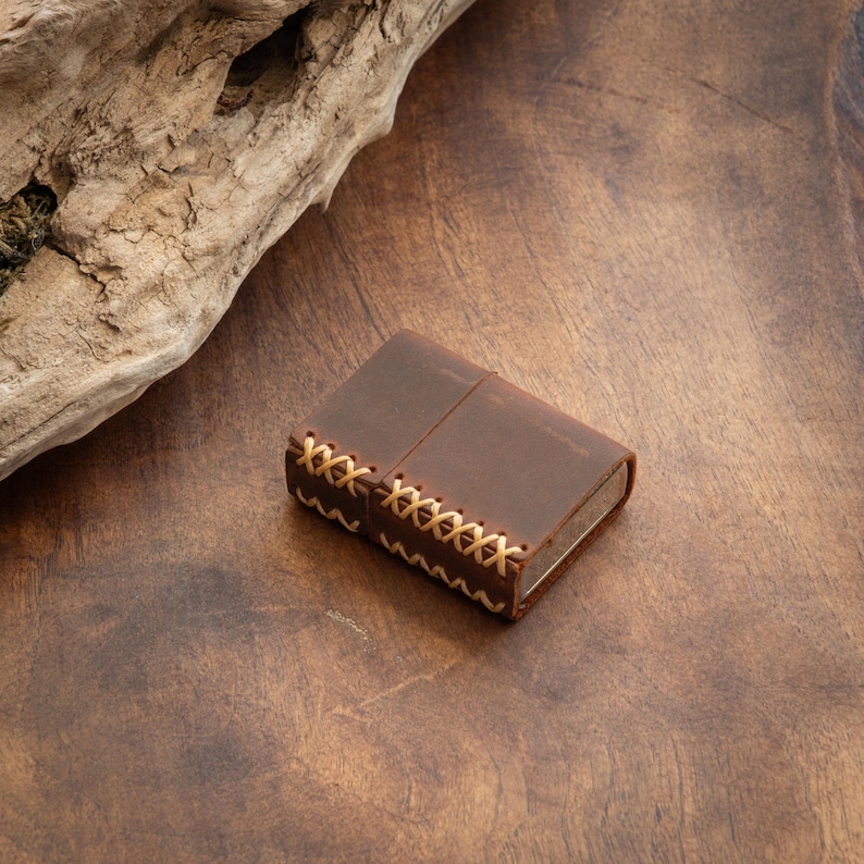 May include: A brown leather lighter case with a stitched design. The case is closed and has a worn look.