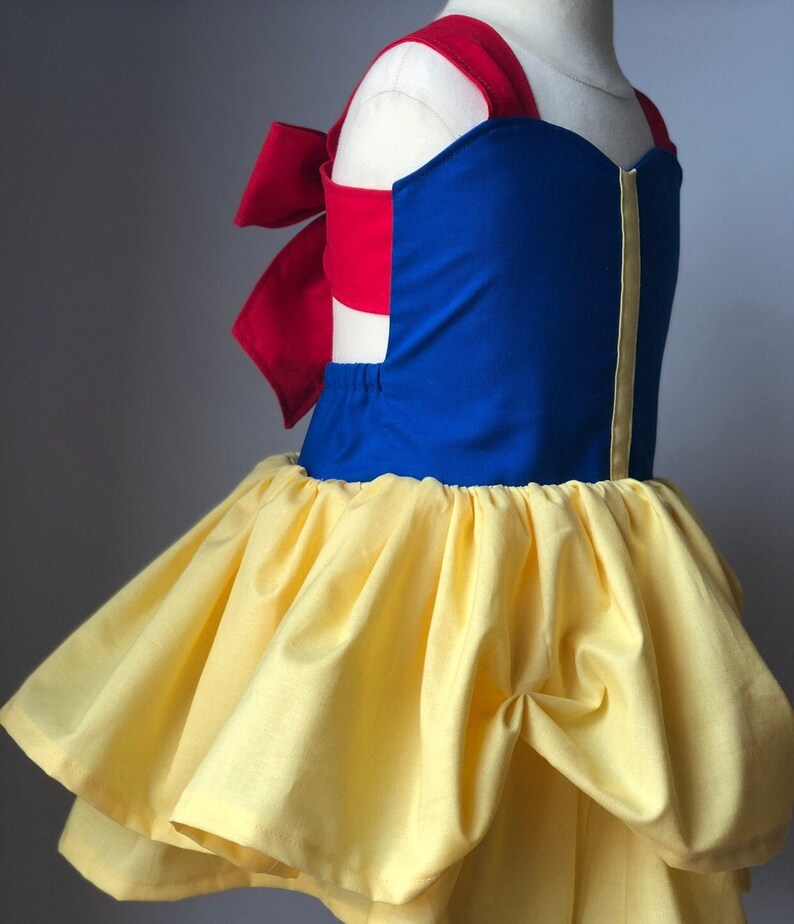 May include: A blue and yellow dress with a red bow on the back. The dress has a sweetheart neckline and a full skirt.