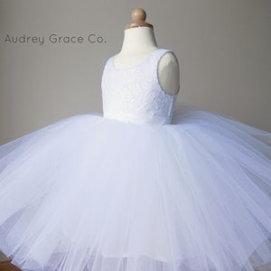 Op de afbeelding: Witte tule jurk met een kanten lijfje en een satijnen band. De jurk is op een witte mannequin. Audrey Grace Co.