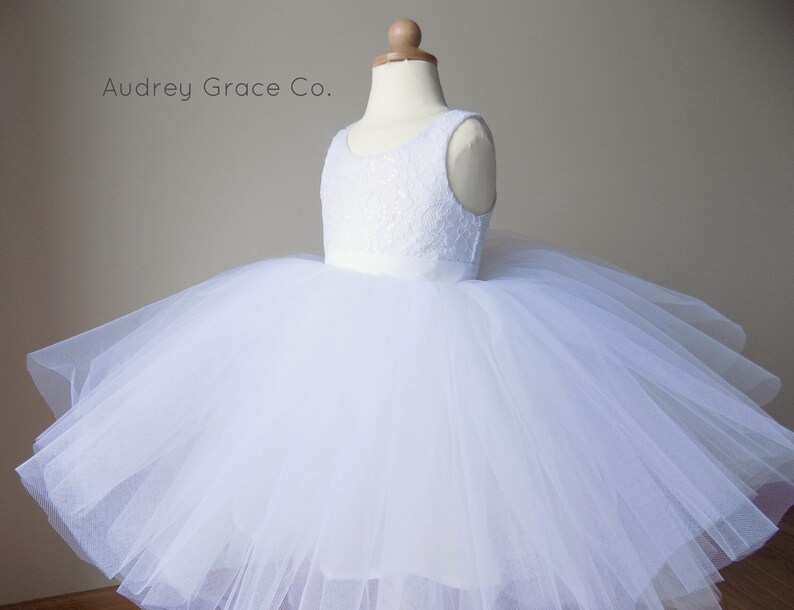 Op de afbeelding: Witte tule jurk met een kanten lijfje en een satijnen band. De jurk is op een witte mannequin. Audrey Grace Co.