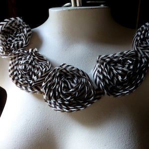 May include: A brown and white striped fabric necklace with five large fabric flowers. The flowers are arranged in a circular pattern around the neck.