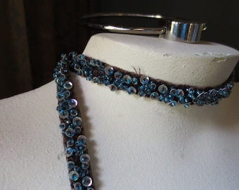 May include: A brown choker necklace with blue iridescent sequins. The necklace is on a white mannequin bust.
