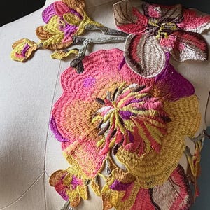 May include: A large floral embroidery applique featuring vibrant shades of pink, magenta, yellow, and gold thread. The design consists of multiple interconnected flower blossoms and buds arranged in a cascading vertical pattern across the torso.