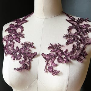 May include: Two pieces of dark purple floral lace applique. The lace features intricate designs of leaves and flowers. The lace is displayed on a mannequin, showcasing the potential for garment embellishment. The lace is a deep, rich shade of purple.