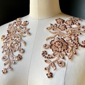 May include: Two ornate, rose gold floral appliques with sequin and bead embellishments. The appliques feature detailed floral and leaf patterns, ideal for embellishing garments or accessories. The appliques are displayed on a mannequin.