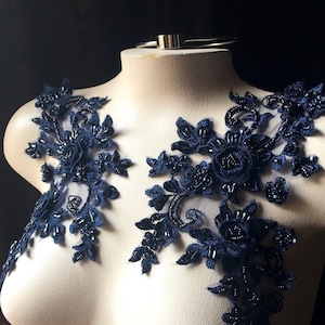 May include: Two navy blue lace appliques with beaded embellishments. The appliques are on a white mannequin bust.