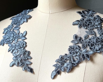 May include: Two matching floral lace appliques in a dark teal color. The appliques are displayed on a mannequin, showcasing the intricate floral and leaf patterns. The lace has a delicate, textured appearance.