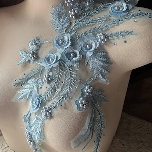 May include: Light blue floral applique with pearl embellishments. The applique features delicate flowers and leaves, perfect for adding a touch of elegance to clothing or crafts.