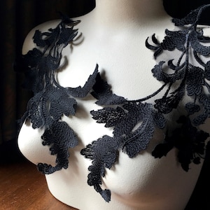 May include: Black lace applique with a floral design. The lace is delicate and intricate, with a variety of shapes and sizes of flowers. The lace is perfect for adding a touch of elegance to any project.