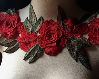 May include: Red embroidered floral applique with green leaves. The applique is on a white mannequin.