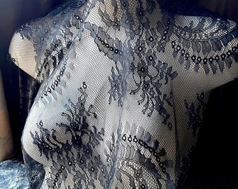 May include: Black lace fabric with a delicate floral pattern. The lace is draped over a mannequin form.