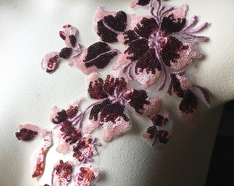 Puede incluir: Una aplicación floral rosa y burdeos con lentejuelas. La aplicación está hecha de tela delicada y presenta una variedad de formas de flores.