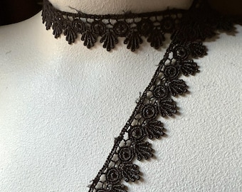 May include: A brown lace trim with a scalloped edge. The lace is delicate and intricate, with a floral pattern.