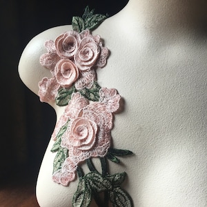 Puede incluir: Aplicación floral bordada con rosas rosas y hojas verdes. El diseño está fijado a un maniquí, destacando los detalles del bordado y la tela. Esta aplicación decorativa es ideal para embellecer ropa o accesorios.