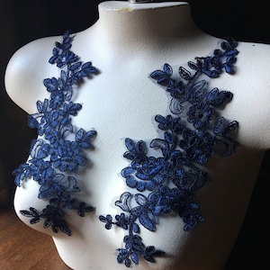 May include: Two navy blue floral lace appliques displayed on a white mannequin. The lace is delicate and features intricate floral designs.