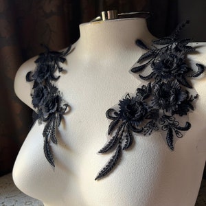 May include: Two black lace appliques with floral designs. The appliques are on a white mannequin bust.