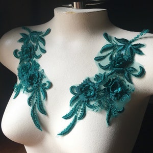 May include: Two teal green floral lace appliques with a delicate mesh backing. The appliques feature intricate floral designs with raised 3D details.