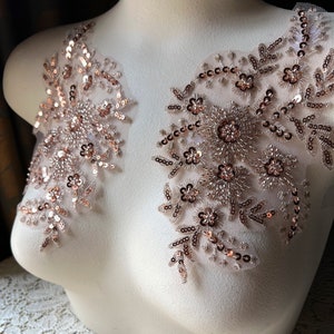 May include: Two rose gold sequined lace appliques with floral designs. The appliques are on a white mannequin bust.