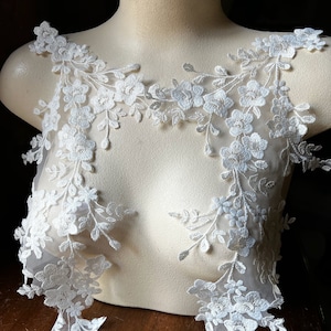 May include: White lace applique with floral designs. The lace is delicate and intricate, with small flowers and leaves. The applique is perfect for adding a touch of elegance to any project.