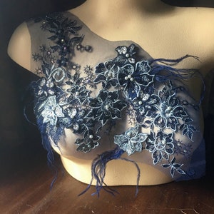 May include: Navy blue lace applique with embroidered floral designs, pearls, and feathers. The applique is displayed on a mannequin, showcasing the intricate details and textures of the embellishments. This decorative piece is suitable for various craft projects.