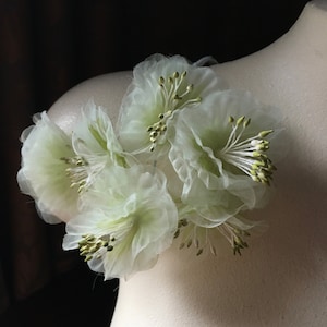May include: A cluster of delicate, white, sheer fabric flowers with green centers. The flowers are arranged in a circular shape and are attached to a white surface.