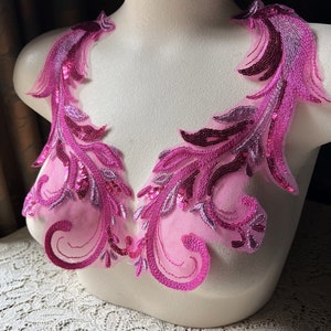 Könnte beinhalten: Zwei rosa und violette Pailletten-Spitzenapplikationen mit floralem Muster. Die Applikationen befinden sich auf einer weißen Mannequin-Büste.