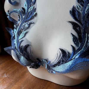 Könnte beinhalten: Blaue und türkisfarbene florale Spitzenapplikation mit Pailletten. Die Spitze ist auf einem durchsichtigen Netzstoff.