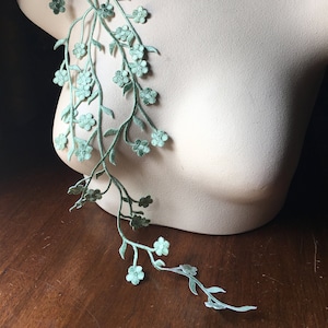 May include: A green floral applique featuring delicate flowers and leaves. The applique is ideal for adding a touch of elegance to clothing, accessories, or home decor.