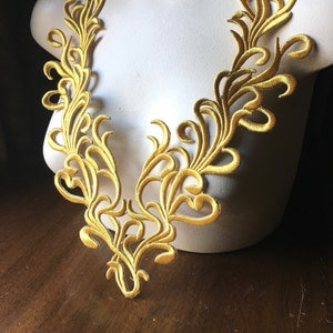 Op de afbeelding: Gouden geborduurde kantbies met een delicaat bloemenmotief. Deze bies is perfect om een ​​toets van elegantie aan elk project toe te voegen.