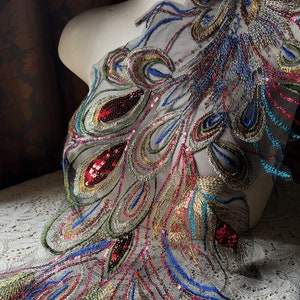 May include: Peacock feather design embroidered applique with sequins in shades of gold, blue, green, and red on a sheer mesh fabric.