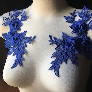 May include: Two blue floral lace appliques featuring intricate flower designs. These appliques are ideal for adding a touch of elegance to garments, accessories, or home décor projects.