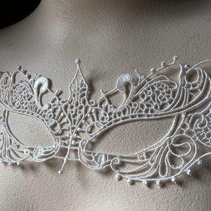 May include: White lace masquerade mask with intricate floral designs. The mask is delicate and features a delicate pattern.