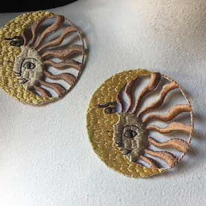 May include: Two embroidered patches featuring a sun and moon design. The sun and moon are yellow and gold with brown rays. The sun and moon have a stylized face with black eyes.