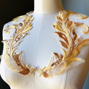 Könnte beinhalten: Gold- und bronzefarbene Applikation mit Pailletten in floralem Design. Die Applikation wird auf einer Schneiderpuppe präsentiert. Das Design hat einen zarten Netzrücken und ist mit Pailletten und Perlen verziert, was einen schimmernden Effekt erzeugt.